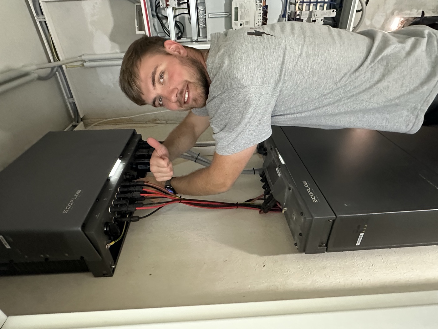 Monteur von Root Elektrotechnik im Firmen-Shirt bei der Montage eines Stromspeichers, Daumen hoch